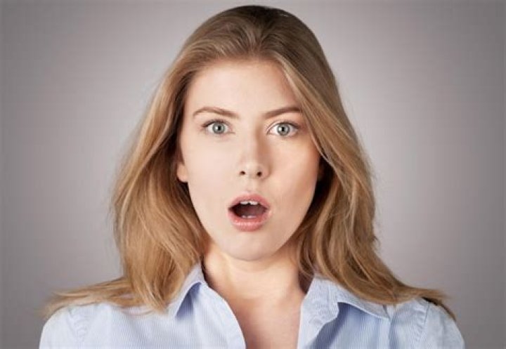 A startled looking woman using her phone to call 911 while driving