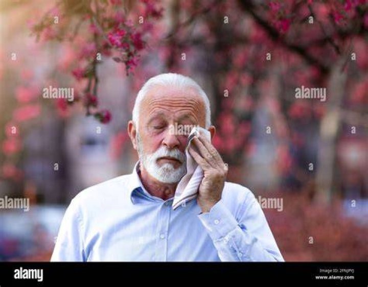 Senior man wiping eyes with tissue outdoors