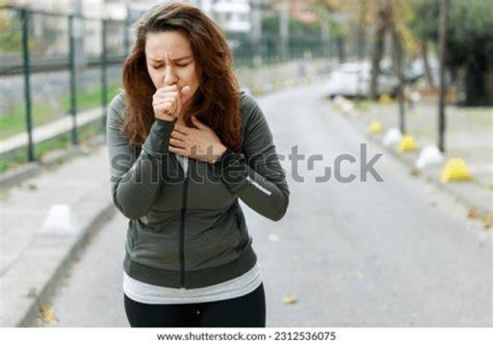 Young sporty woman coughing while walking on the street. Athlete woman affected by air pollution during running training